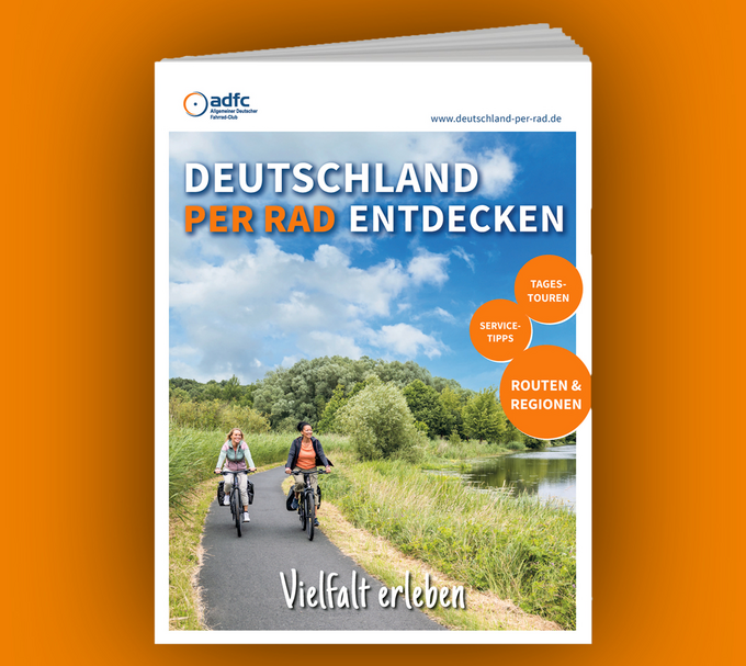 Zwei Radfahrerinnen auf einem asphaltierten Radweg durch eine naturbelassene Flusslandschaft